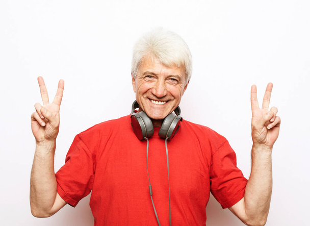 a portrait of smile old man with headphones show victory sign, over white background - Фото, зображення