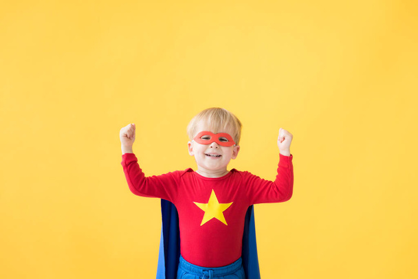 Portrait of superhero child. Super hero kid against yellow paper background. Happy child wearing red mask and cape of superhero. Children dream and imagination concept - Photo, Image