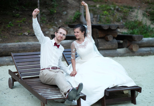 la novia y el novio en las tumbonas levantan las manos, celebran la boda y la felicidad futura. - Foto, imagen