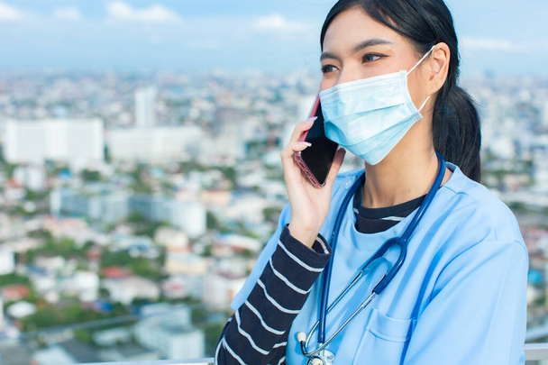 Portrait of young asian woman doctor healthcare professional in blue uniform standing in hospital.. Doctor using tablet ,mobile for work.Close up head shot on rooftop. - Фото, зображення