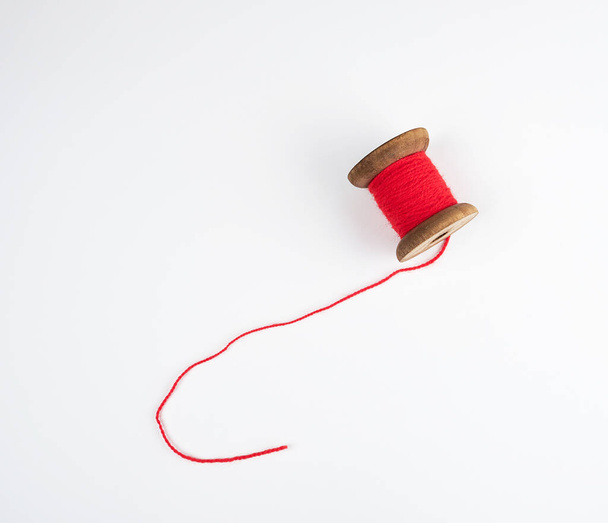 wooden bobbin with red wool threads on a white background, close up - Fotó, kép