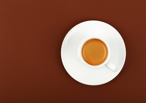 Close up one white cup full of espresso coffee on saucer over brown paper background, elevated top view, directly above - Fotoğraf, Görsel