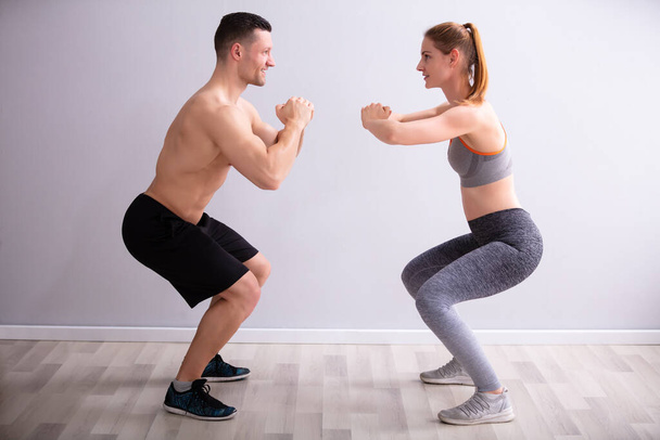 Side View Of Happy Fitness Couple In Sportswear Doing Squat Exercises At Gym - Fotografie, Obrázek