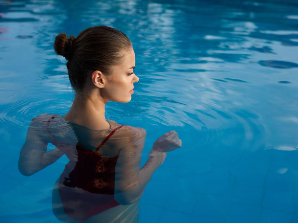 mujer bonita en traje de baño se encuentra en la baldosa de la piscina en vista trasera de agua transparente - Foto, imagen