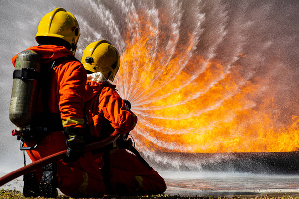 İki itfaiyeciden oluşan bir itfaiye ekibi oksijen tankı sırtında su dökerek açık hava felaketlerinin yaşandığı bölgede cesur ve sorumluluk sahibi büyük turuncu bir ateşe göğüs gerdiler. - Fotoğraf, Görsel