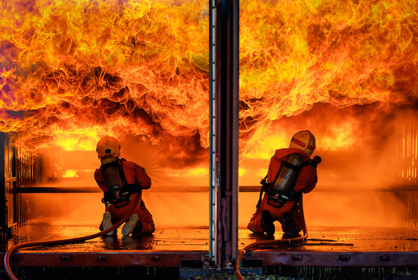 İki itfaiye ekibi, oksijen tüplü üniforma giyip su dökerek dar felaket bölgesinde cesur ve sorumluluk sahibi iki büyük turuncu ateşe göğüs gerdiler.. - Fotoğraf, Görsel