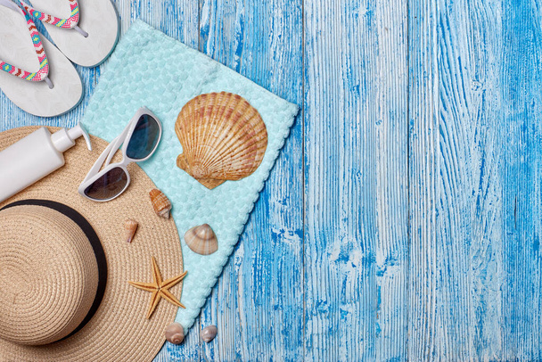 Beach accessories: white female flip flops, straw hat, sunglasses, sunscreen on blue wooden background. Top view with copy space. Concept of sea vacation and travel. Summer background, Protection from uv - 写真・画像