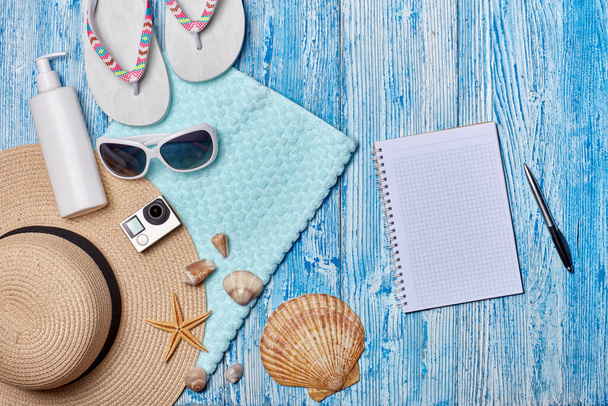 Beach accessories: flip flops, straw hat, sunglasses, sunscreen, towel, blank notebook on blue wooden background. Top view with copy space. Concept of planning vacation and travel. Summer background - Foto, immagini
