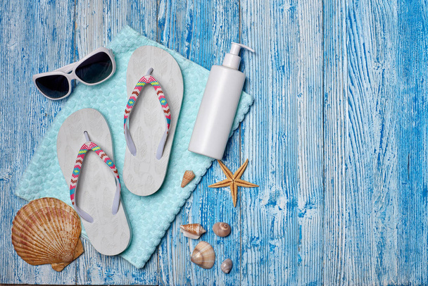 Beach accessories: white female flip flops, sunglasses, sunscreen on blue wooden background. Top view with copy space. Concept of sea vacation and travel. Summer background, Protection from uv - 写真・画像