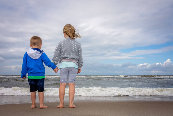 Little boy and girl standing on the sand waiting for wave to come on the beach in summer - Photo, Image