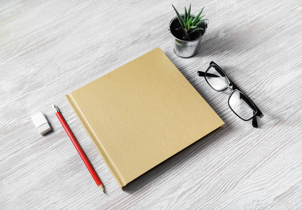 Blank stationery template. Closed blank sketchbook, glasses, pencil, eraser and plant on light wood table background. - Photo, image