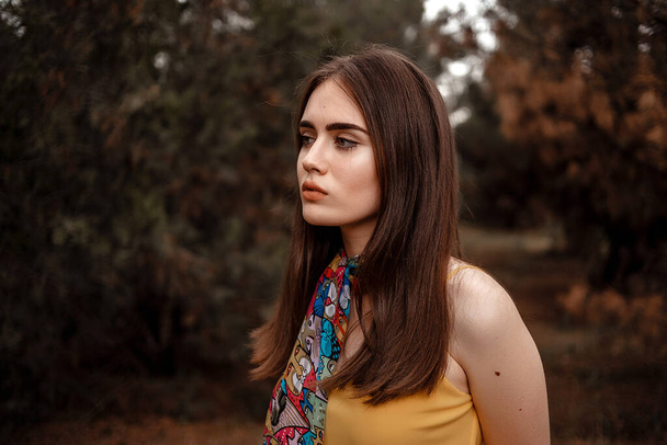 portrait of a young beautiful girl in a yellow dress with a colorful scarf standing in the woods - Foto, Bild