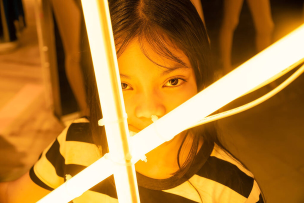 Das Mädchen mit einer Glühbirne in Orange auf der Vorderseite., Ein junges asiatisches Mädchen mit einer Leuchtstofflampe. - Foto, Bild