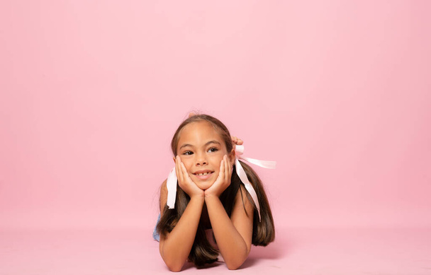 Beautiful smiling little girl lying on the floor isolated over pink background. - Fotó, kép