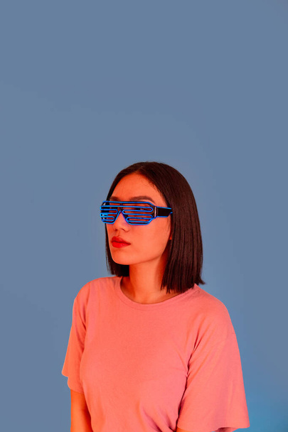 Junge asiatische Frau trägt Kopfhörer und futuristische LED-Brille isoliert abgeschnittene Werbung Kopierraum Hintergrund - Foto, Bild