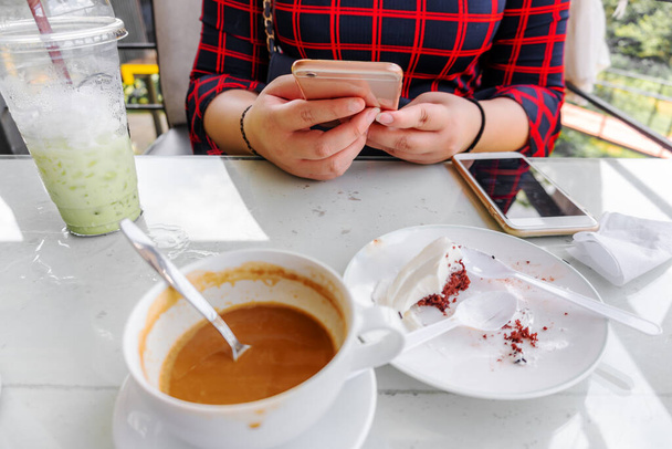 Junge Frauen nutzen Smartphone-soziales Netzwerk mit Cappuccino-Kaffee und Eismilch Grüntee und Schokoladenkuchen im Café Entspannungskonzept erschöpft - Foto, Bild