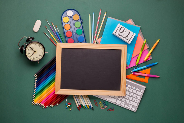Blank blackboard and stationery accessories: pencils, pens, other office supplies on green background. Top view, copy space.  School accessories for children's  education and development - Photo, Image