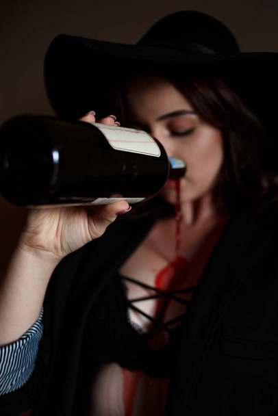 beautiful young girl in black underwear and black pantsuit in the entrance drinking wine or drink from a bottle. selective focus on the bottle - Φωτογραφία, εικόνα