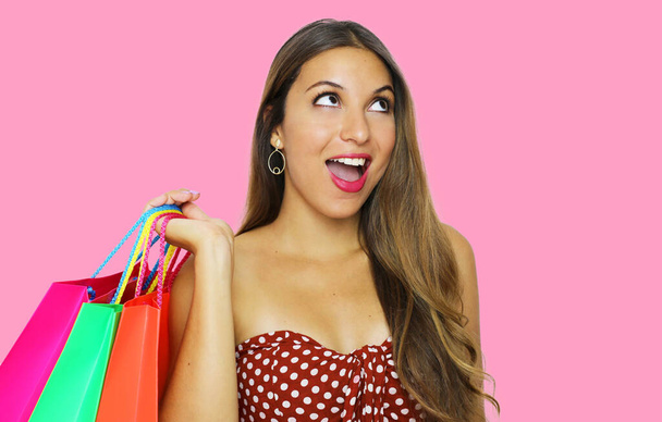Excited fashion woman holdings shopping bags and looks up the copy space on pink background. - Foto, immagini