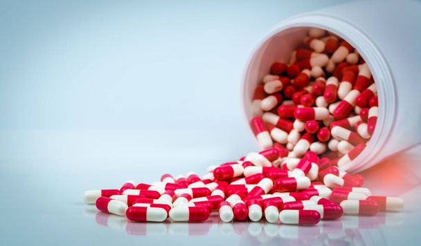 Red-white capsule pills on white table on blurred background of drug bottle. Antibiotics drug resistance. Antimicrobial capsule pills. Pharmaceutical industry. Pharmacy. Global healthcare concept. - Fotografie, Obrázek