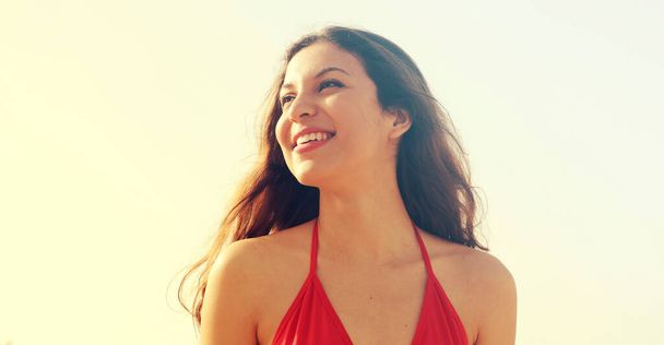 Beautiful brunette in red bikini smiling confident and looking to the side on the beach on a sunny day low angle banner crop - Fotó, kép