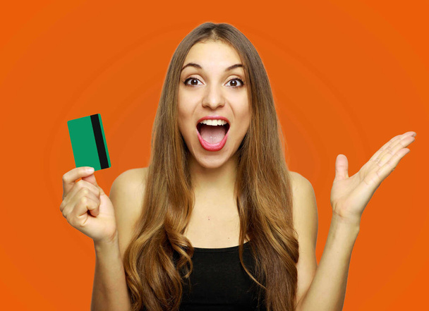 Happy excited amazed young woman holding credit card over orange background - Foto, Imagen