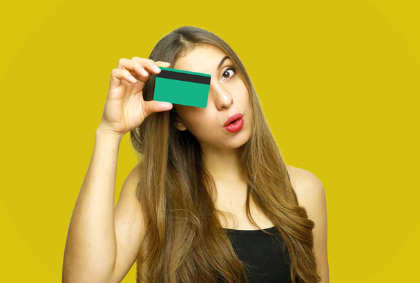 Portrait of a pretty young woman holding credit card at her face isolated over yellow background - Fotografie, Obrázek