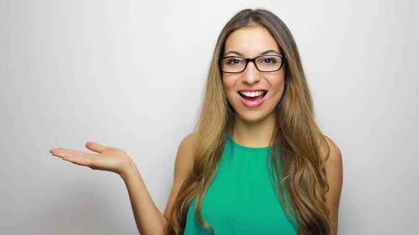 Excited elegant girl with glasses showing at white background with copy space. Young beautiful happy smiling and laughing woman shows your product on her hand. - Zdjęcie, obraz