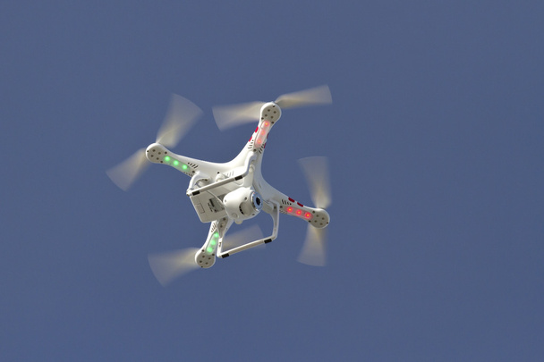 pequeño helicóptero no tripulado con una cámara flotando en el cielo azul
 - Foto, Imagen