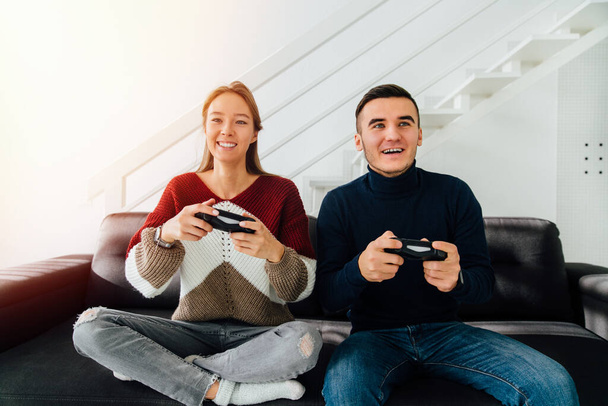 Pretty girl and a guy playing video games online, sitting on couch together, dressed in warm casual clothes. At home. - 写真・画像