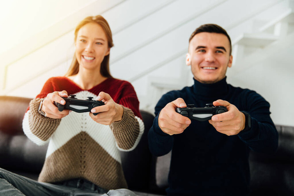 Young happy friends, guy and girl playing video games with joysticks, sitting on couch at home. - Φωτογραφία, εικόνα