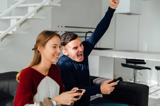 Excited happy guy celebrate winning, raised his fist up after playing computer games with beautiful girlfriend, sitting on sofa at home. - Foto, Imagem