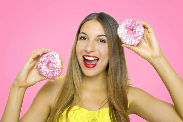 Primer plano de la niña sosteniendo donuts mira a la cámara en el fondo rosa. - Foto, Imagen
