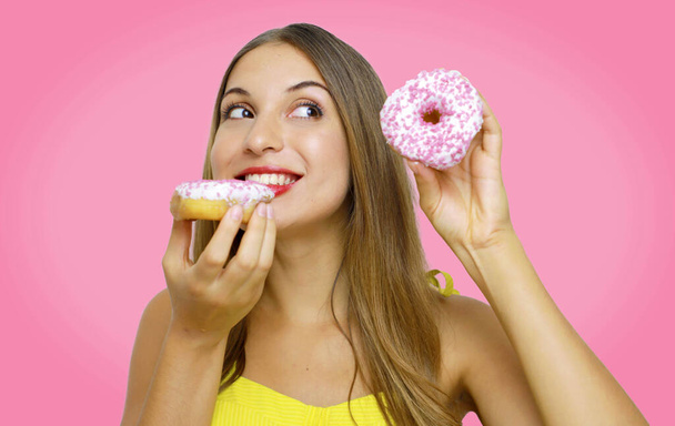 Close up portrait of a satisfied pretty girl eating donuts isolated over pink background. - Fotografie, Obrázek