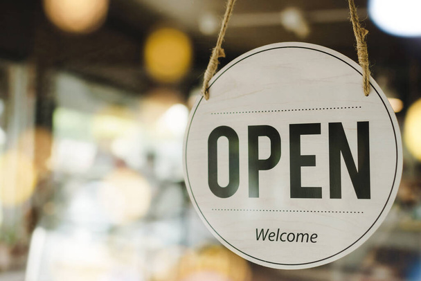Open text on vintage sign board hanging on glass door with bokeh light in modern cafe shop reopen after coronavirus quarantine is over in restaurant ready to service, small business owner concept - Photo, image