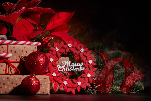 Christmas decoration with Red Poinsettia flowers (Euphorbia Pulcherrima), fir branch and gift boxes on a dark background.  Christmas background with copy space. Greeting card. - Foto, immagini