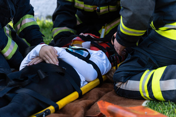 Het slachtoffer van een auto-ongeluk ligt op een brancard. brandweerlieden helpen hem. - Foto, afbeelding