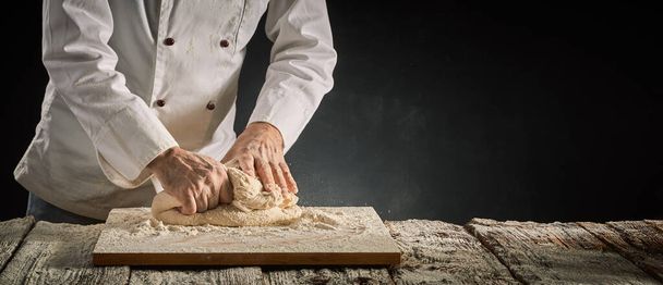 Hands of a chef or baker kneading raw dough on an old wooden board in a rustic panorama banner with copy space - Foto, immagini