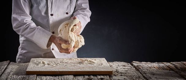 Baker of chef kneading a large portion of dough with his hands during preparation over a floured wooden board in a rustic panorama banner with copy space - Photo, Image