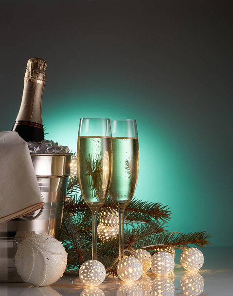 Still life with champagne bottle standing in a bucket with ice, two full champagne flutes, LED lights garland  and Christmas ornaments. Christmas and New Year celebration background - Φωτογραφία, εικόνα