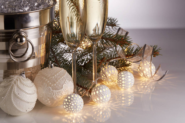 Still life with champagne bottle standing in a bucket with ice, two full champagne flutes, LED lights garland  and Christmas ornaments. Christmas and New Year celebration background - Fotoğraf, Görsel