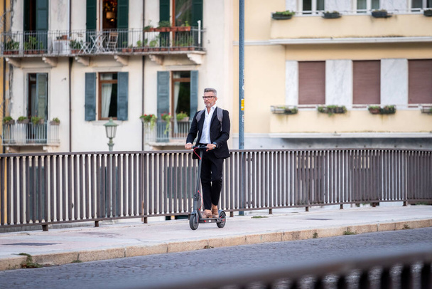 Komea liikemies puku ratsastus sähkö skootteri kun työmatkalla töihin kaupunkiin. Ekologisen liikenteen käsite - Valokuva, kuva