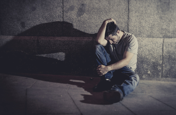 depressed young man sitting on street ground with shadow on concrete wall - Photo, Image
