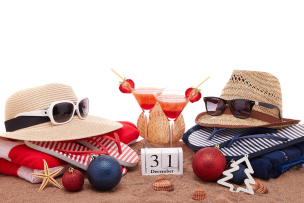 Beach accessories (flip flops, straw hats, seashells, sand, sunglasses), two glasses of cocktail, christmas ornaments on white background. New Year. Winter  vacation  in warm countries, beach holiday - Foto, Bild