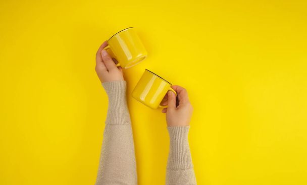 two yellow ceramic cups are supported by a female hand on a yellow background, copy space - 写真・画像