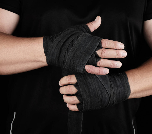 man wraps his hands in black textile bandage for sports, black background, copy space - Foto, Bild
