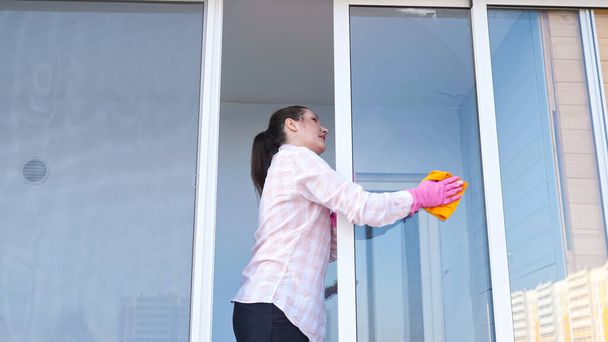 Жінка з Брюнета в рукавичках з розпилювачем і ганчірка миє вікно, зовні. - Фото, зображення