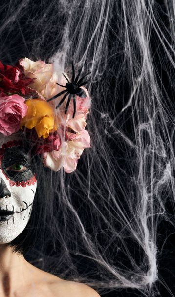 girl with black hair is dressed in a wreath of multi-colored roses and makeup is made on her face Sugar skull to the day of the Dead, close up - Foto, Imagem
