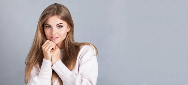 portrait of a beautiful young woman in a white sweater and a blue shirt on a gray background - Photo, image