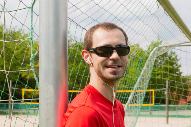 Friendly young sportsman with sunglass and earphones outdoor in a park - Foto, afbeelding